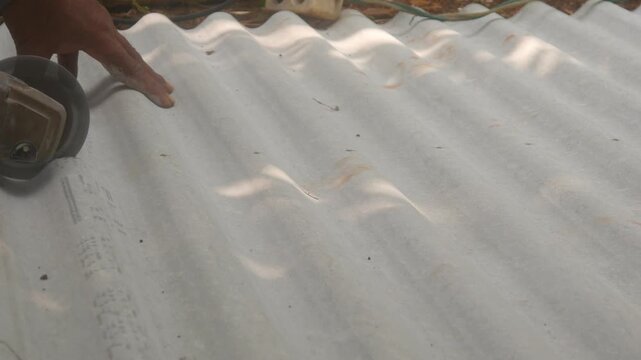 A construction worker uses a hand grinder to cut asbestos or fiber cement roofing sheets.