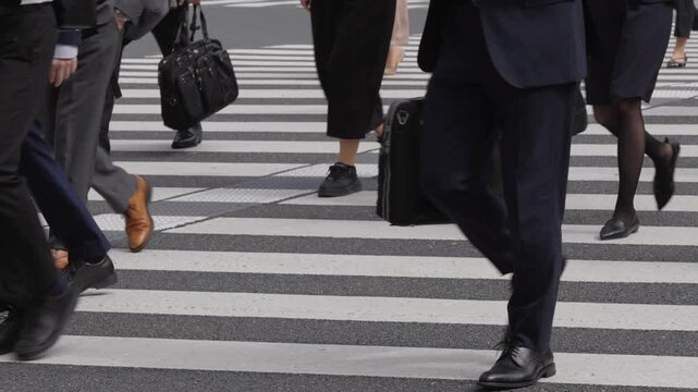 横断歩道を渡り朝の通勤するビジネスマンたちの後ろ姿の足元のスローモーション　東京