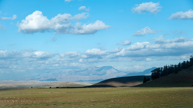Wide panoramic view of the Middle Atlas Mountains in Morocco with green plains and a blue sky filled with white clouds on a sunny day showcasing a vast natural landscape