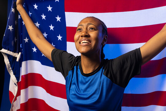African American woman holding US flag with grommet, posing in studio wearing blue athletic shirt