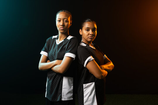 African American female teammates standing in studio wearing black-white jerseys, rim lights, turf