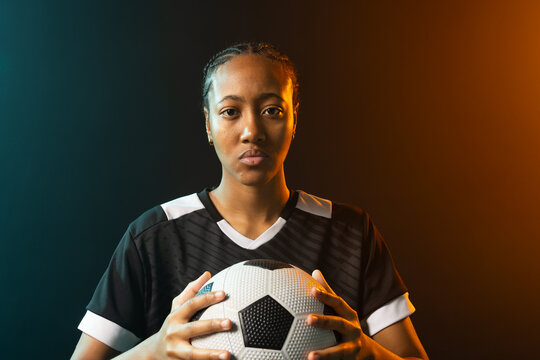 Female athlete holding soccer ball with both hands at chest in studio, wearing black jersey