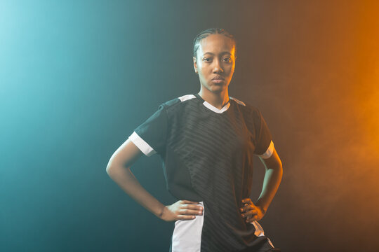 African American woman standing in studio wearing black jersey and shorts under teal-amber lights