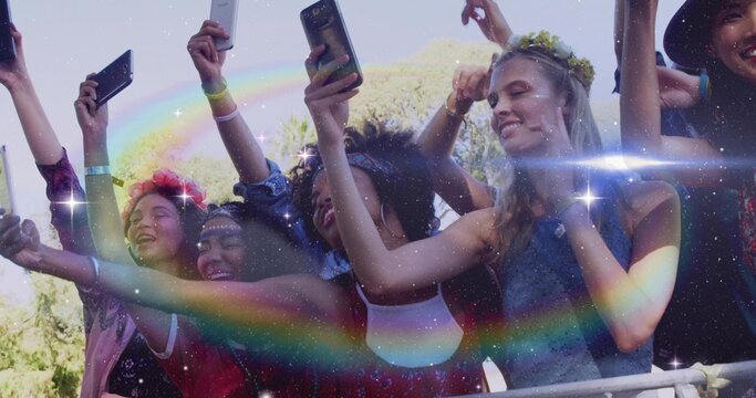 Cheering front-row crowd raising phones at metal barrier in park, wearing tanks and flower crowns