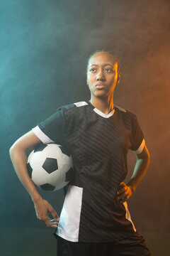 African American woman standing holding soccer ball on studio turf wearing black jersey