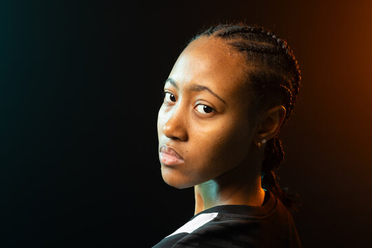 African American woman studio posing, wearing top with white-stripe, studs, teal amber rim lighting