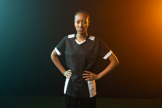 African woman standing hands on hips on turf in studio, wearing black jersey and shorts