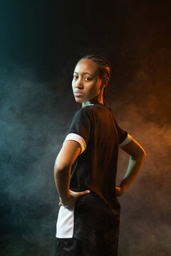 Female athlete posing, looking over shoulder in studio with teal and amber haze, wearing jersey
