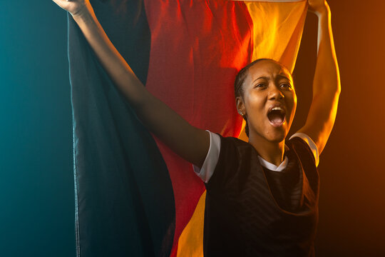 Woman holding large tricolor flag, shouting in studio wearing dark jersey and hoops