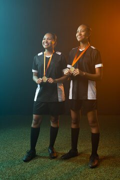 African female team standing side by side on turf wearing black white jerseys and gold medals