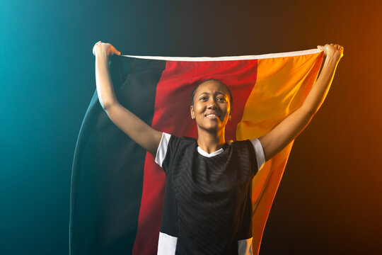 African American woman wearing black sports shirt holding tricolor flag overhead in studio lighting