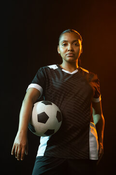 African American woman posing in studio in black jersey holding ball under teal orange lighting