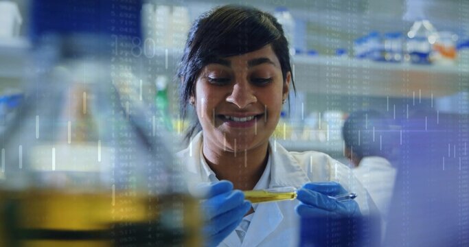 Smiling scientist in white lab coat blue gloves holding test tube at bench, showing data overlay