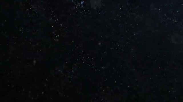 Dark abstract background with numerous small, light specks creating a grainy texture.