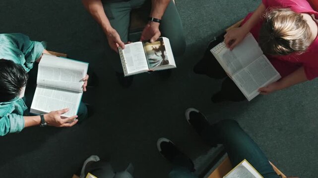 Top down view of prayer reading at bible book and sitting in circle with bible book on laps. Aerial view of diverse people looking at book while studying with faith, trust and hope, calm. Symposium.