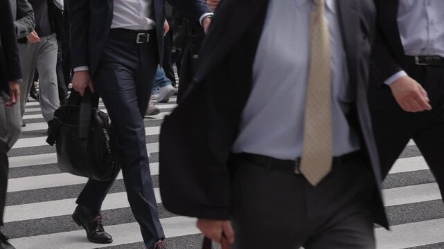 横断歩道を渡り朝の通勤するビジネスマンたちの後ろ姿の足元のスローモーション　東京