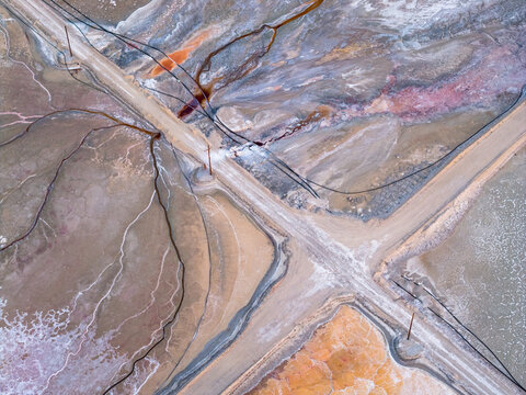 Aerial view of Searles Lake featuring colorful mineral deposits, salt flats, and industrial pipes crossing dirt roads in San Bernardino County, California, United States.