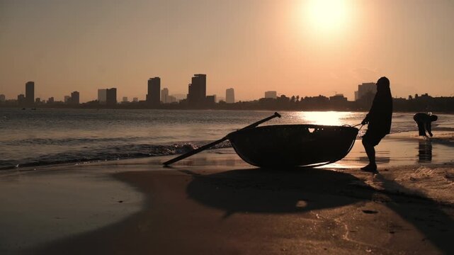 Sunset Silhouette On Da Nang Beach, Fisherman Pulling Coracle Boat Across Wet Sand, Orange Glow, Distant City Skyline, Gentle Waves And Reflective Shoreline, Tranquil Atmosphere