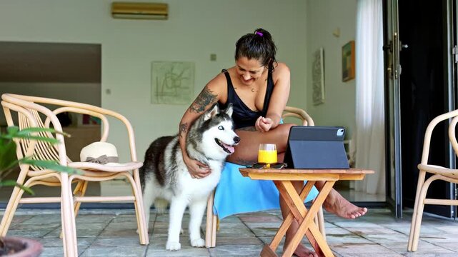 Digital nomad woman petting her siberian husky dog while working on tablet