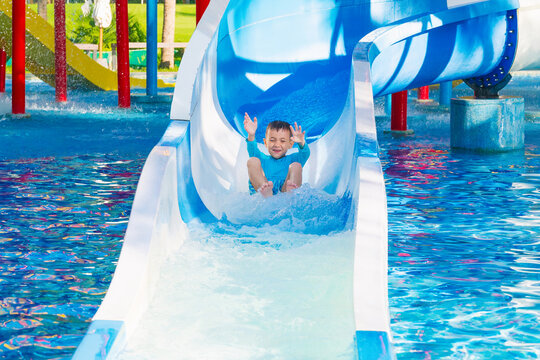 Caucasian cute happy child boy rides a water slide in a water park in summer vacation. Children's aquapark in pool at the resort