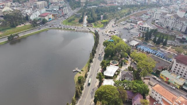 Vietnam, Da Lat Aerial View Xuan Huong Lake And Roundabout, Drone Surveying Lakeside Park, Calm Water Reflection, Treelined Promenade, Light Morning Traffic And Surrounding Buildings