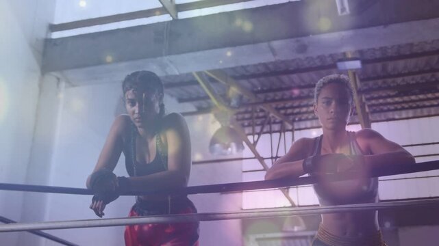 Post sparring round, two female boxers leaning on ropes amid lens flare, preparing for next round