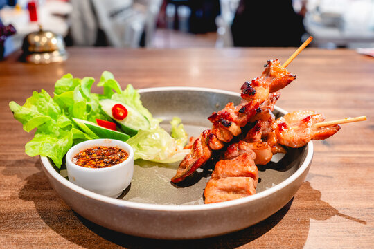 Grilled marinated pork skewers served with spicy dipping sauce and a side of fresh greens and cucumber slices.