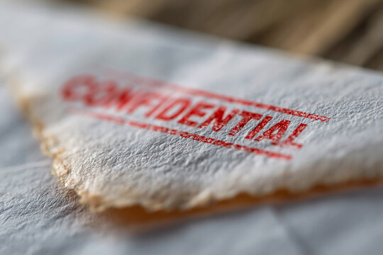 Confidential stamp marks old, textured paper. Faded edges suggest vintage or archival use. Red ink contrasts sharply against the paper's tone. Blurred background emphasizes the stamp's importance
