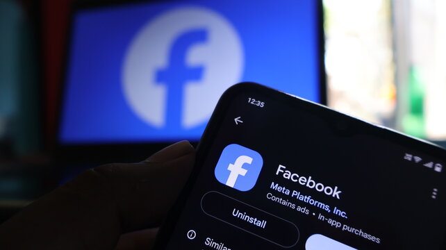 A hand holding a smartphone with the Facebook app on the screen