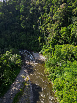 Aerial view of the river flowing through the lush tropical rainforest of Mount Leuser National Park with rocky banks and dense green trees Kecamatan Darul Hasanah, Aceh, Indonesia.