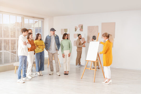 Female guide showing painting to people at exhibition in art gallery