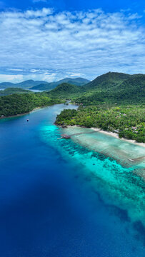 Aerial view of We Island featuring turquoise waters, a wooden pier, and lush tropical hills under a cloudy sky Sabang City, Aceh, Indonesia.