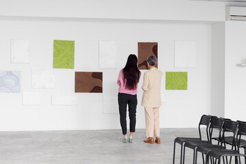 Fototapeta premium Female guide with visitor near paintings at exhibition in art gallery, back view