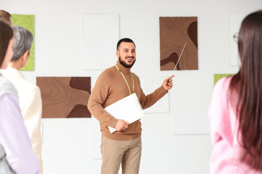 Male guide showing paintings to people at exhibition in art gallery