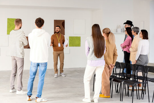 Male guide with people near paintings at exhibition in art gallery