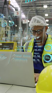 Vertical video: Tech at laptop in plant checking metrics while AR charts appearing, yellow hard hat
