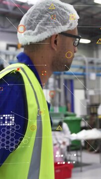 Vertical video: Factory worker gripping rail holding orange cart inspecting machines with HUD data