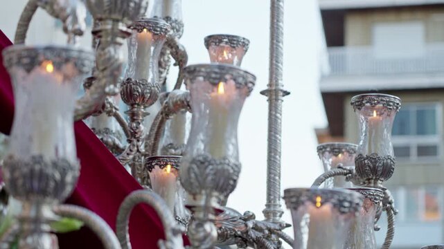 Ornate silver candelabra illuminated by lit candles, part of a traditional religious procession in Spain, symbolizing faith and devotion