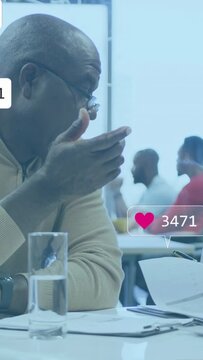 Vertical video: Senior reading docs in biz meeting, incoming bubbles floating over docs to review
