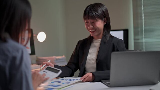 Asian businesswomen collaborating on financial report during overtime