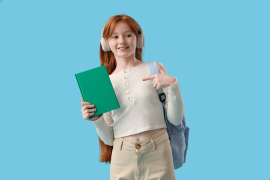 Teenage redhead girl pointing at notebook on blue background