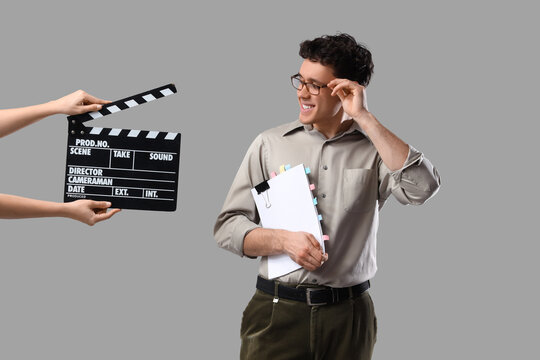Male screenwriter holding scenario and female hands with movie clapper on grey background