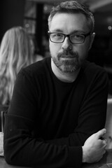 Obraz premium Black and white portraits of man in his 40s wearing glasses indoors. Candid lifestyle series with crossed arms, beard, and confident expression.
