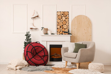 Naklejka premium Inflatable sled, comfortable armchair and fireplace in interior of light living room