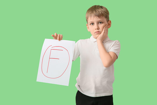 Sad schoolboy holding paper with bad grade on green background