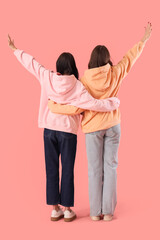 Fototapeta premium Teenage girls hugging on pink background, back view