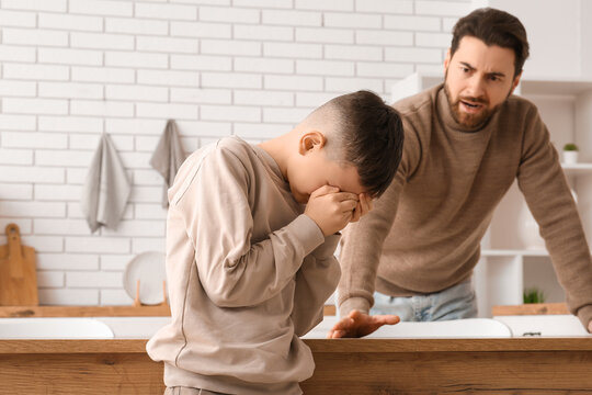 Young father and his sad little son squabbling in kitchen