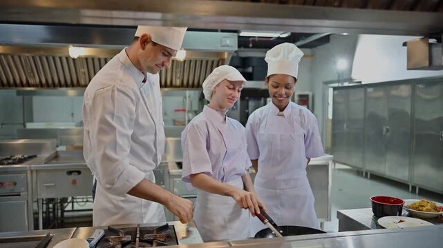 Professional male chef teaching two female culinary students in modern commercial kitchen