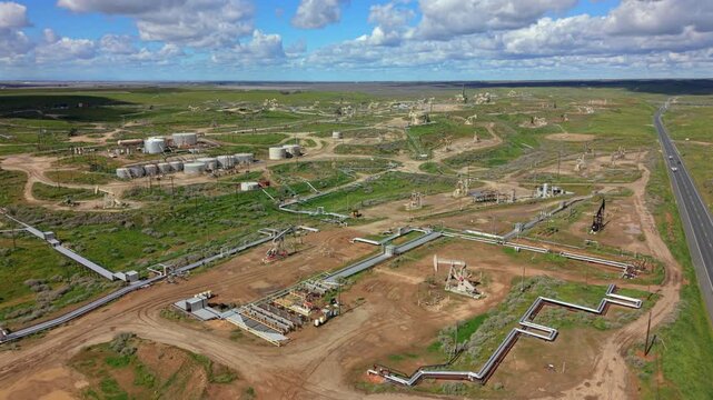 Aerial drone view processing hub with large storage tanks and dense pipeline grid, service roads and wellheads interlaced with green fields, industrial scale emphasized by textures, tanks