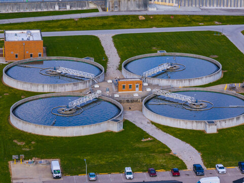 Aerial view of four circular wastewater treatment clarifier tanks with rotating bridges and brick utility buildings surrounded by green lawns in Indianapolis, Indiana, United States.